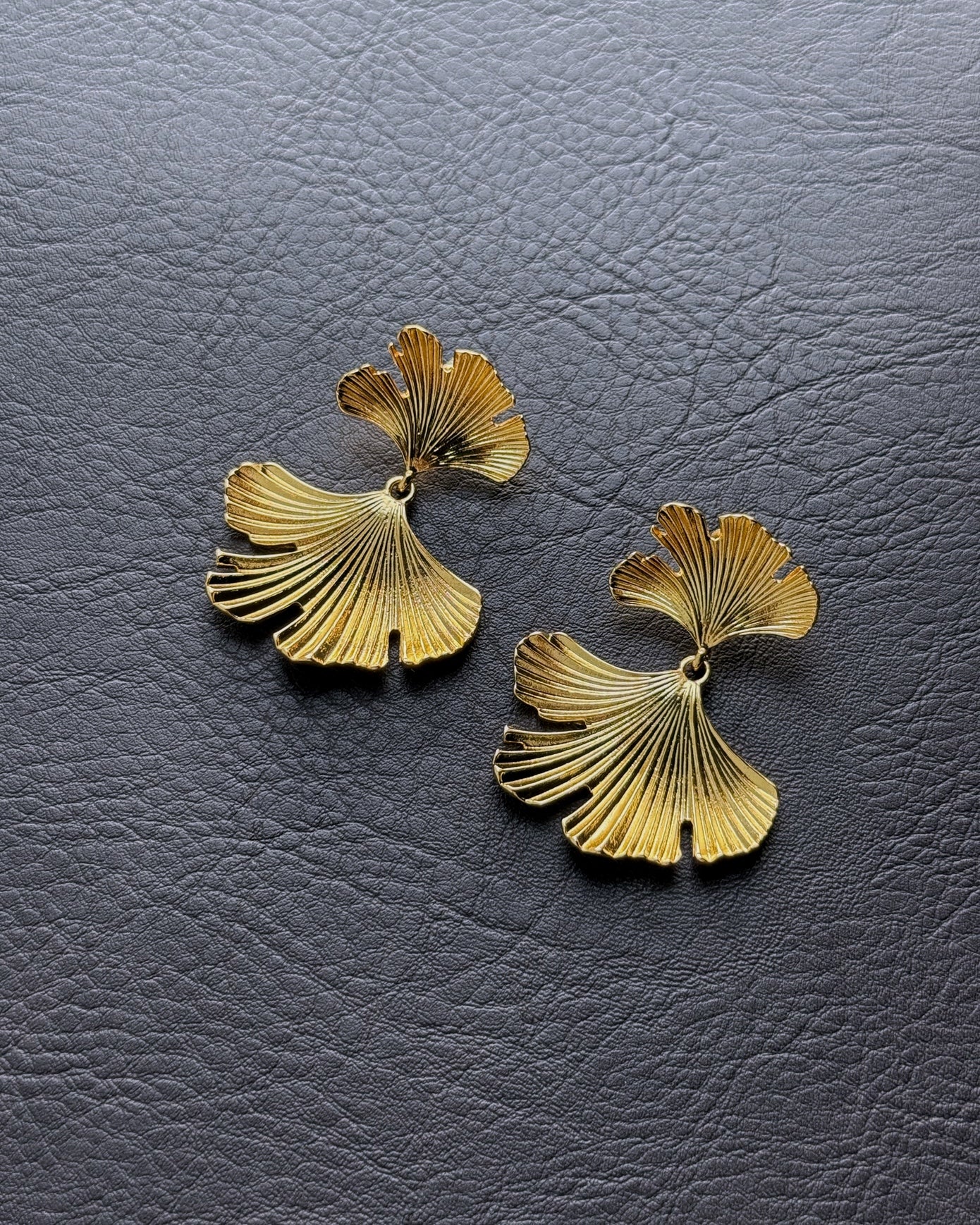 Layered gold ginkgo leaf earrings on leather background