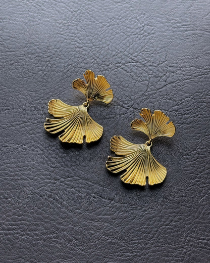 Layered gold ginkgo leaf earrings on leather background